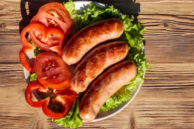 Grilled sausages with fresh vegetables on wooden table. Top view