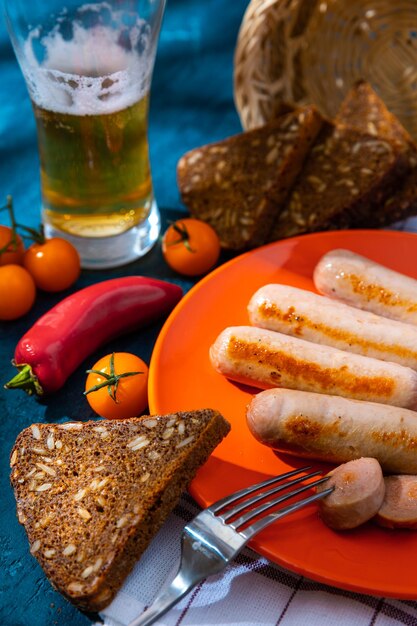 Grilled sausages with a glass of beer on a blue background closeup Sliced bread yellow tomatoes