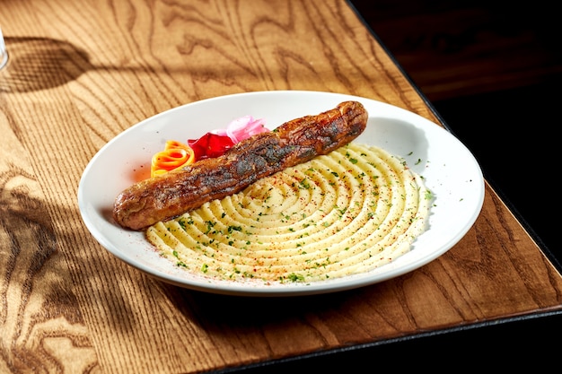 Grilled sausages with mashed potatoes in a white plate on a wooden table. Currywurst