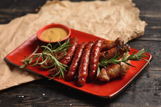 Grilled sausages with rosemary and mustard sauce. In a red plate on a wooden table