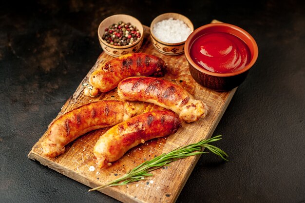 Grilled sausages with spices, ketchup and rosemary on a stone table, ready to eat