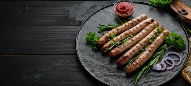 Grilled sausages with tomato sauce on a black stone plate BBQ Top view Free copy space