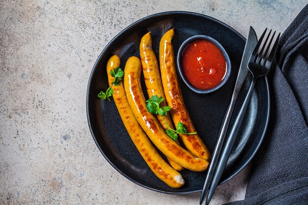 Grilled sausages with tomato sauce and herbs on a black plate.