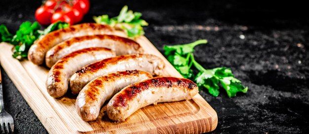 Grilled sausages on a wooden cutting board with parsley and tomatoes