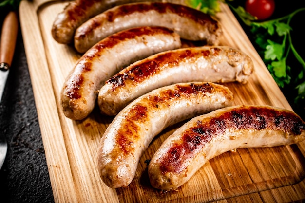 Grilled sausages on a wooden cutting board with parsley and tomatoes