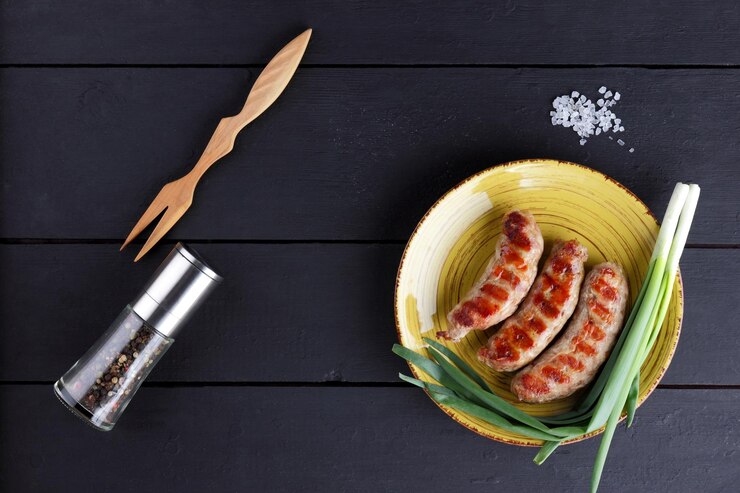 Жареные сосиски на желтой тарелке Тарелка с мясным блюдом на темном фоне Горячие сосиски со специями и зеленым луком Вид сверху Копией пространства