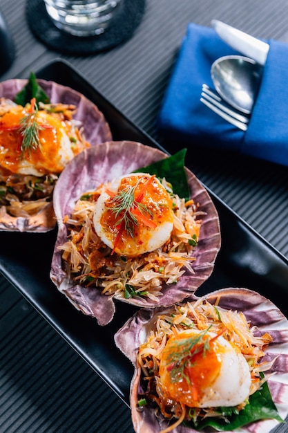 Grilled scallop in shell with spicy pomelo salad served in black plate.