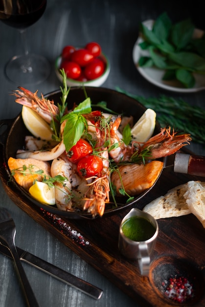 Фото Морепродукты гриль на сковороде на деревянной доске, креветки, лосось, кальмары с приправами и соусом