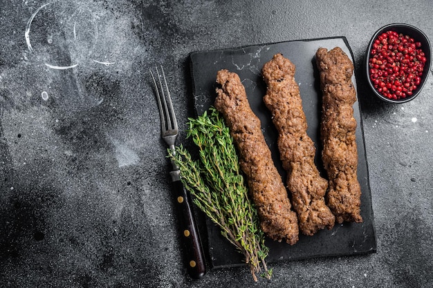 Grilled Shish kebab on a stick, from ground beef and lamb meat, turkish adana kebab. Black background. Top view. Copy space.