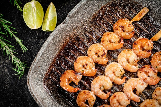 Grilled shrimp on skewers in a frying pan with rosemary and pieces of lime