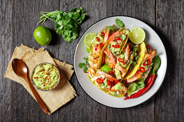 grilled shrimp tacos with cabbage salad, lime and guacamole filling on a plate on a wooden table, flat lay