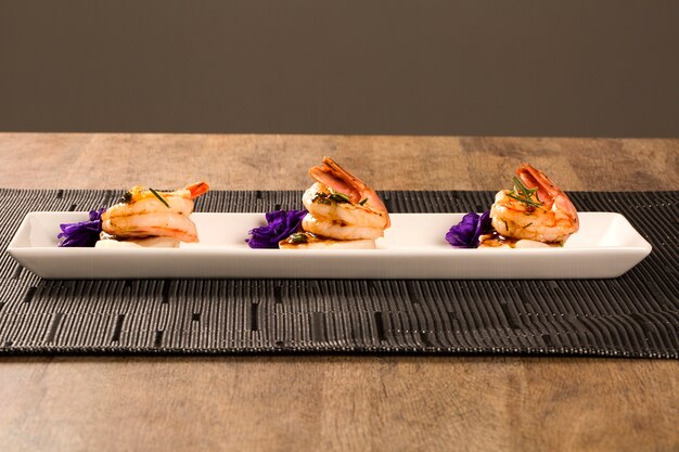 Photo grilled shrimp with raw nail fish on white plate at table