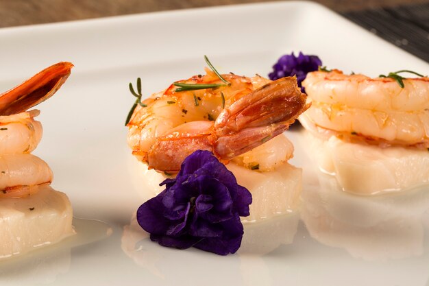 Grilled shrimp with raw nail fish on white plate at table