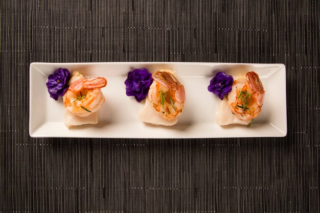 Grilled shrimp with raw nail fish on white plate at table