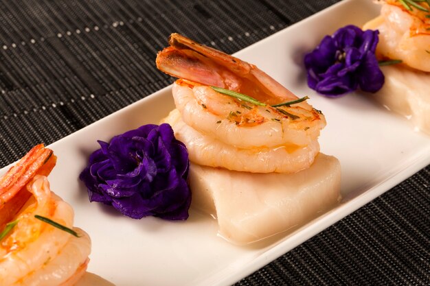 Grilled shrimp with raw nail fish on white plate at table