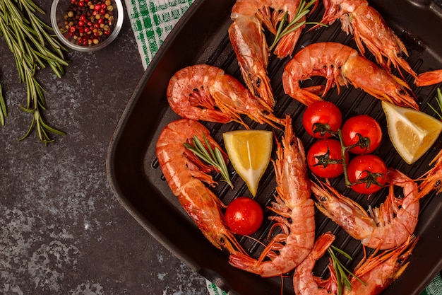 Grilled shrimps with lemon and rosemary on frying pan.