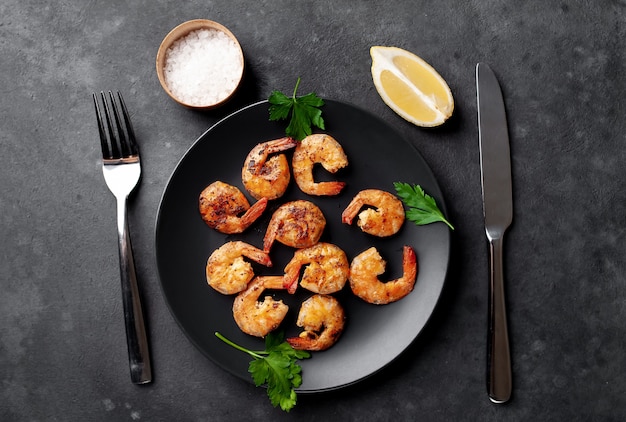 grilled shrimps, with lemons, herbs and spices, served on a black plate on a stone background