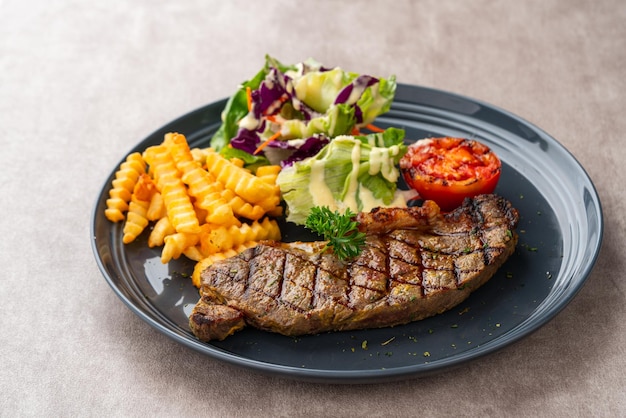 Bistecca di manzo alla griglia con patatine fritte e insalata. servire su piatto nero. spazio negativo.