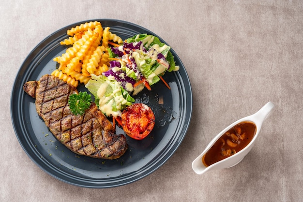 Bistecca di manzo alla griglia con patatine fritte e insalata. servire su piatto nero. spazio negativo.