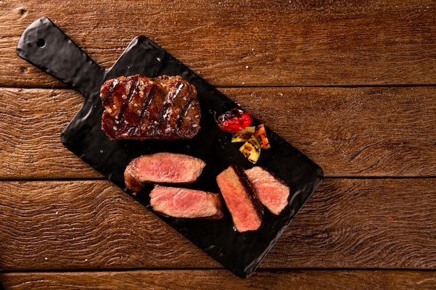 Grilled sliced beef steak on a black cutting board on the wooden table.