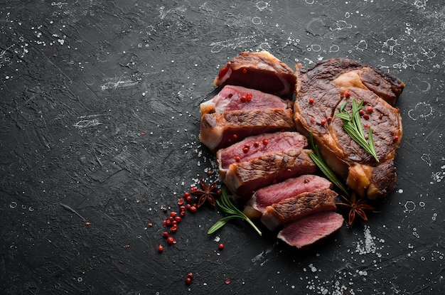 Photo grilled sliced beef steak with rosemary and spices on a black stone background top view free space for your text