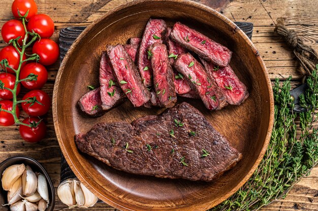 Grilled sliced top blade or denver beef meat steak in a wooden plate with herbs.