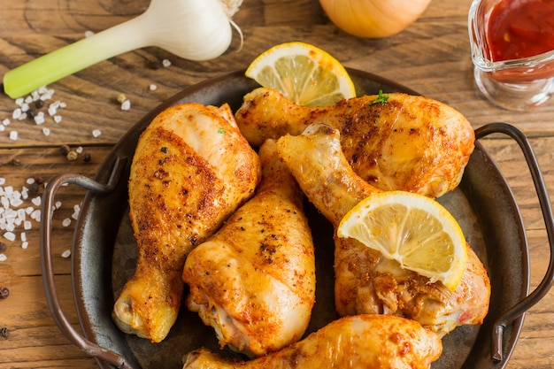 Grilled spicy chicken legs baked with garlic, spices and lemon in a pan onwooden background.