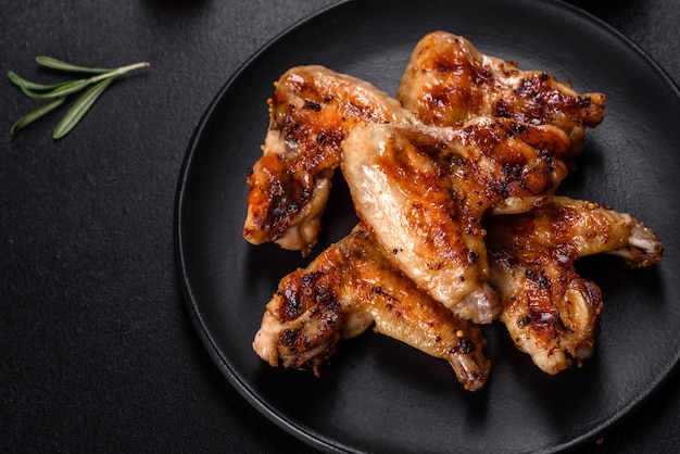 Grilled spicy chicken wings on a dark background with spices and herbs