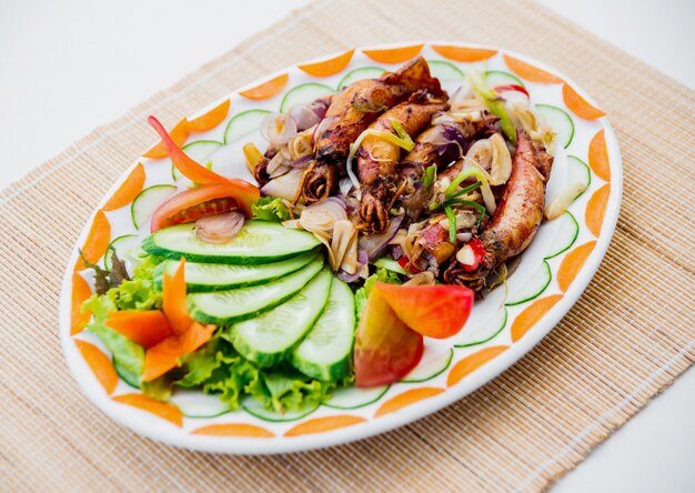 Grilled squid with vegetables on a white plate.