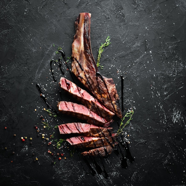 Grilled steak on the bone sliced, herbs and spices on Wooden background. Barbecue. Top view. Free space for text.