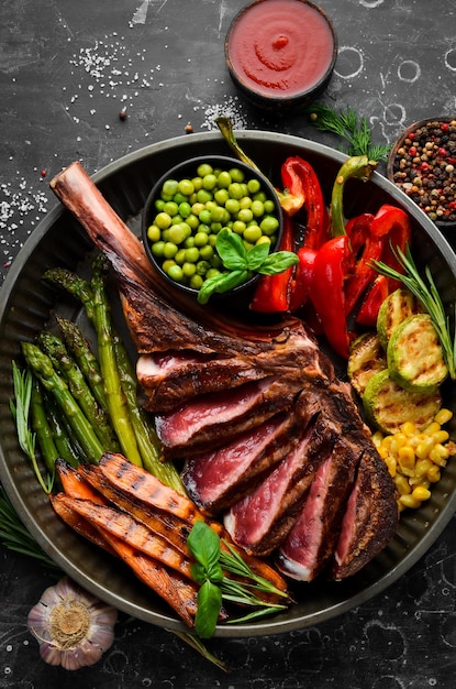 Grilled steak on the bone with grilled vegetables On a black background Top view Free copy space