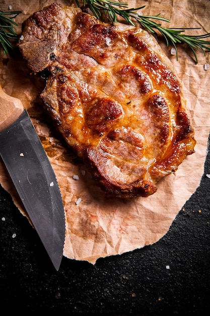 Grilled steak on paper with a knife and a sprig of rosemary