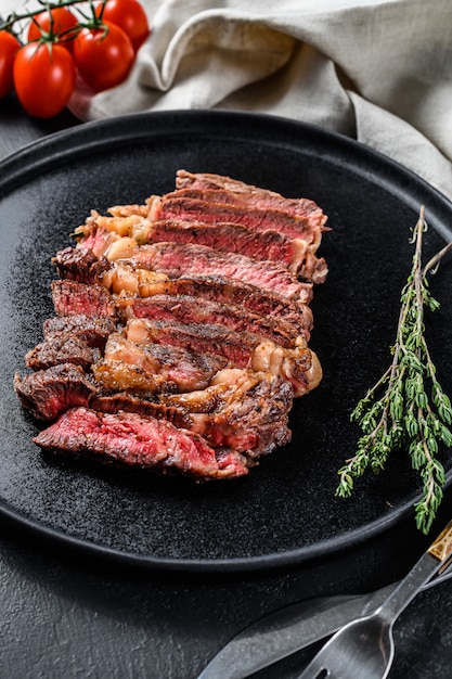 Grilled steak ribeye and spices on a black table