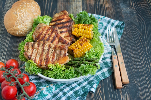 暗い背景の木にスパイス、ハーブ、野菜と丸いボウルのグリルステーキ。肉料理。暗い背景の木。コピースペース。