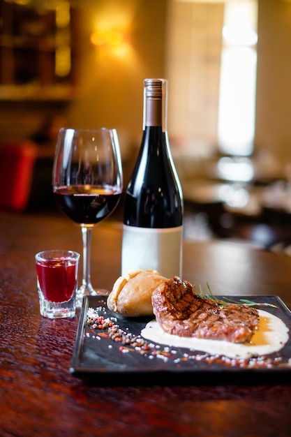 ガラスとワインのボトルと正方形の黒いプレートプレート上のグリルステーキレストランに役立つ美しい料理のコンセプト