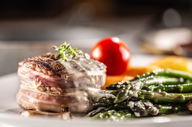 Grilled steak with bacon served on a plate with asparagus and mushroom sauce.