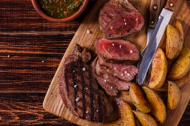 Grilled steak with potato wedges, salsa and spices on dark wooden surface