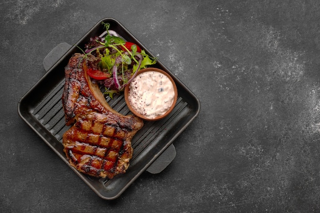 Grilled steak with sauce, vegetables and herbs, on a black frying pan, on a dark table