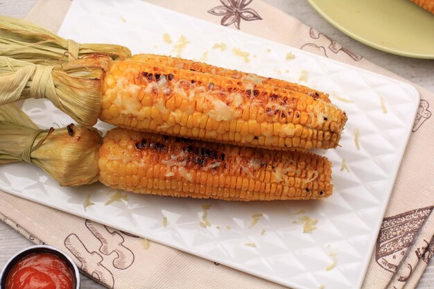 Grilled Sweet Corn with Butter and Shredded Mozarella Served on White Plate