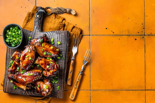 Grilled sweet and sour chicken wings on wooden board Orange background Top view Copy space