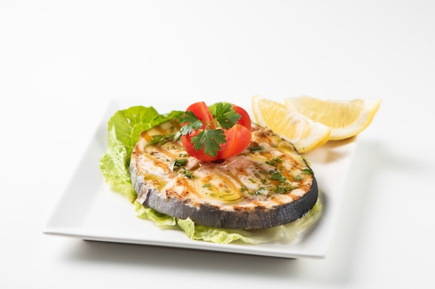 Жареная рыба-меч с салатом и лимоном на белой тарелке. Закрыть вверх