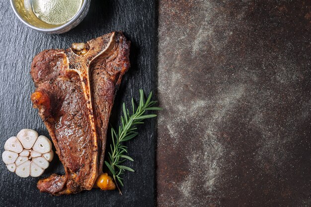 Grilled t - bone steak on black slate plate and old kitchen table