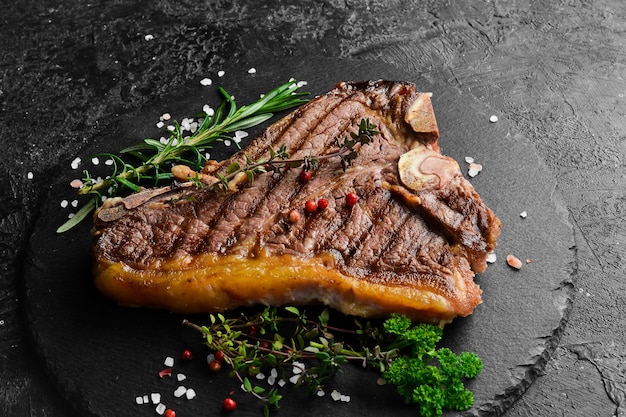 Grilled tbone beef steak steak on a black plate top view on a black stone background