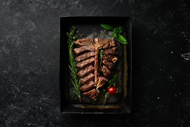 Grilled Tbone steak with spices in a metal baking dish on a black background Top view Rustic style