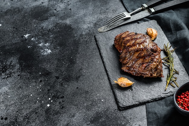 Grilled Top Blade steak on a stone Board, marbled beef. Black background. Top view. Copy space