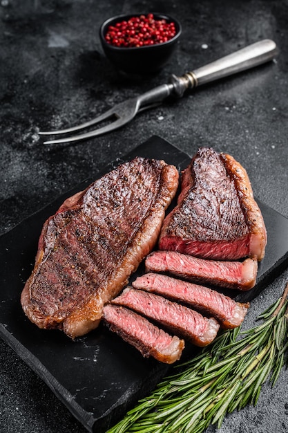 Grilled top sirloin or cup rump beef meat steak on marble board. Black background. Top view.