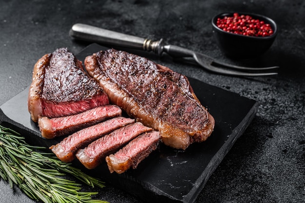 Photo grilled top sirloin or cup rump beef meat steak on marble board. black background. top view.