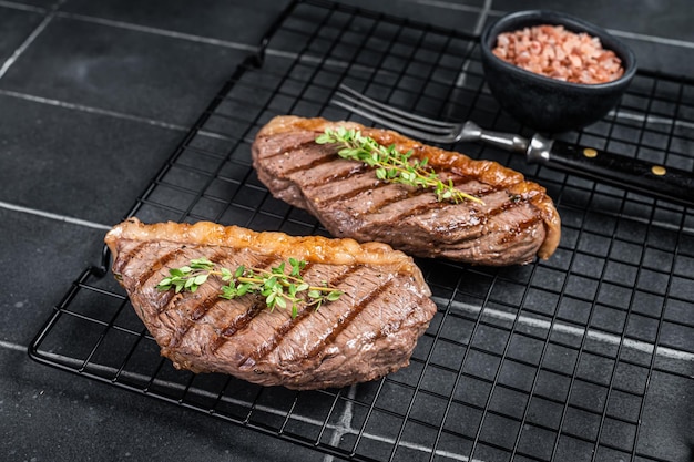 Grilled top sirloin or cup rump beef meat steak on a rack Black background Top view