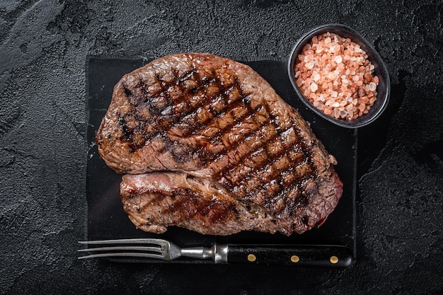Grilled top sirloin or rump steak on a marble board Black background Top view
