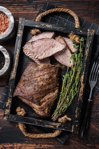 Grilled Tri Tip steak sirloin bottom beef in a tray with herbs Wooden background Top view